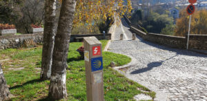 Imatge d'una estaca amb indicadors de senderisme davant la rampa del pont de Sant Joan de les Abadesses